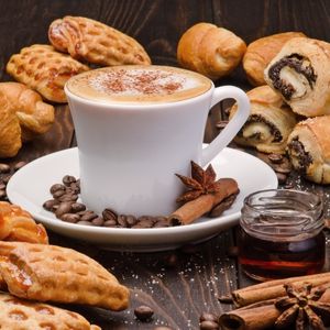 a white cup of coffee on a plate surrounded by coffee beans, spices, baked goods, and maple syrup to show maple syrup in coffee